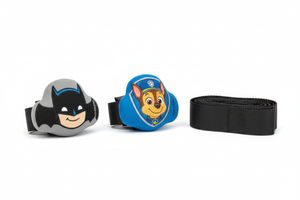 Two BuckleBuddeez infant car seat chest clip covers displayed face-up on a white surface beside a folded harness strap, showing Batman and Paw Patrol Chase character illustrations